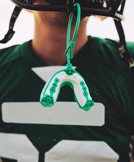 Football helmet with green athletic mouthguard hanging from shield