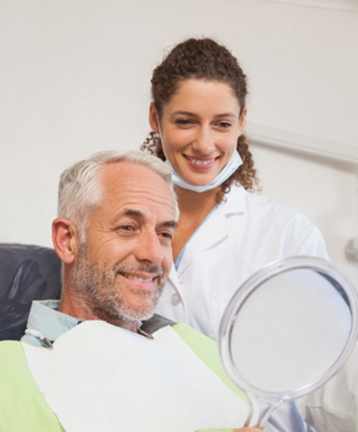 man smiling in mirror at dentist’s office  