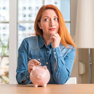 Woman putting coin in piggy bank for cost of veneers in Columbus