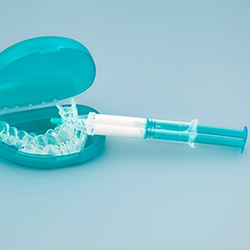 Syringe resting on teeth whitening tray and carrying case