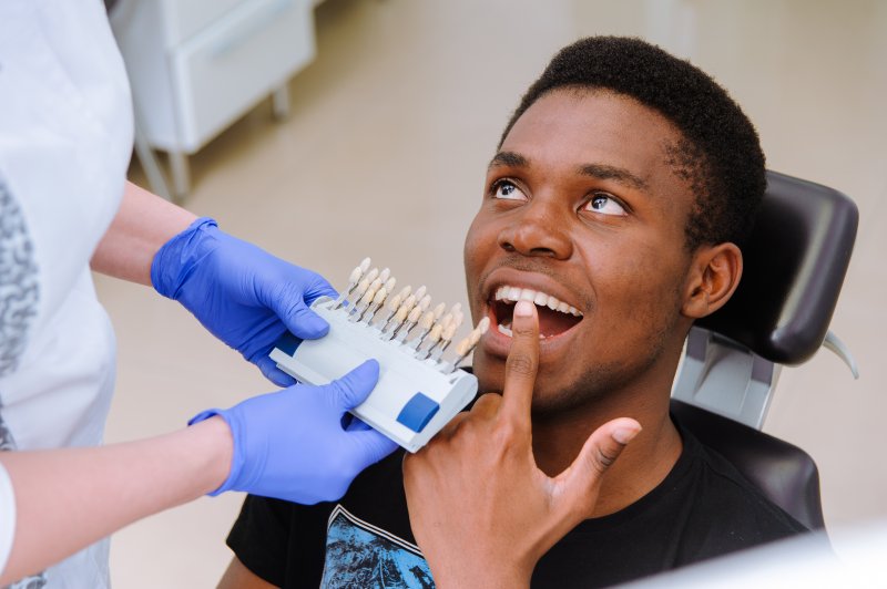 cosmetic dentist holding veneers up to patient’s teeth