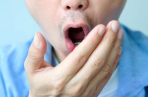 Close up on lower half of the face of a man who is holding his hand in front of his mouth to try to smell his breath