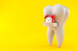 A large fake tooth with a drawer holding a red alarm clock on a yellow background
