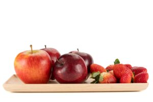 Red apples and strawberries on a wooden dish with a white background