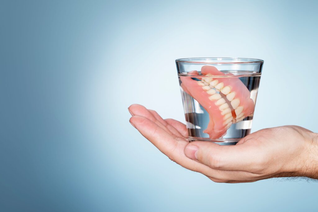 Set of dentures in glass of clear liquid on palm of hand