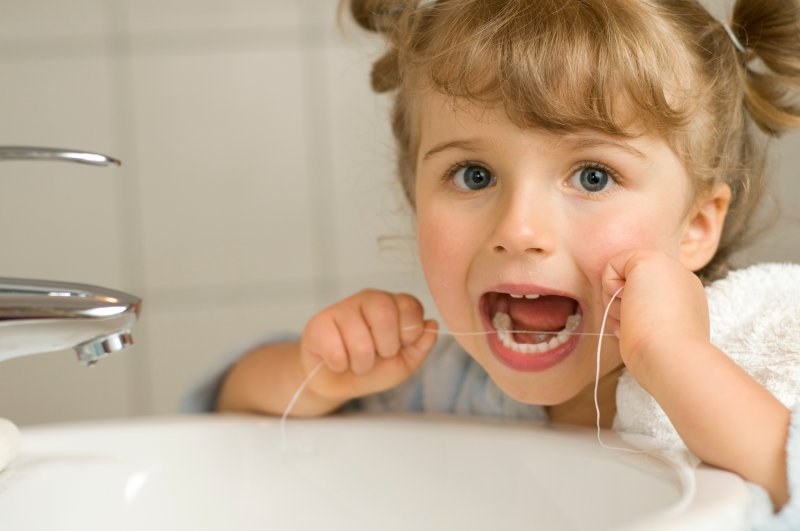 A little girl flossing between her teeth in the bathroom