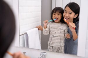 Woman brushing teeth at bathroom mirror with little girl