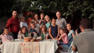 Person taking picture of family gathered around a table outdoors.